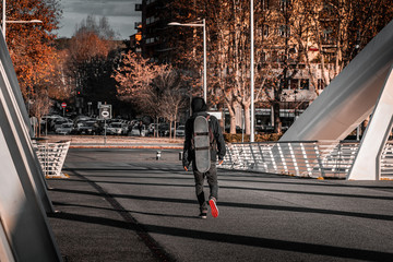 Young teenage skater walking on an industrial footbridge. Tactical extreme back pack with board strapped on. Going to a race. 