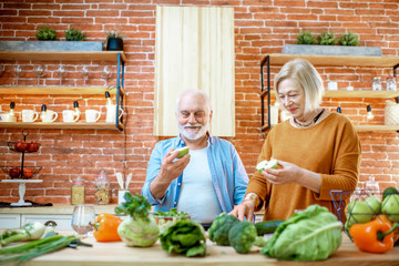 Wall Mural - Cheerful senior couple eating fruits standing together with healthy food on the kitchen at home. Concept of healthy nutrition in older age