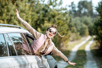 Wall Mural - Young woman enjoying the trip, looking out the car window on a picturesque road in the woods