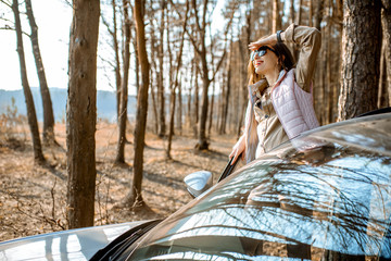 Wall Mural - Young woman traveler enjoying nature while traveling by car in the picturesquare forest with lake