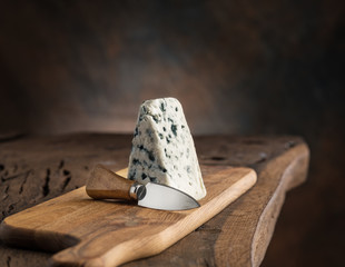 Wall Mural - Piece of blue cheese and cheese knife on the wooden board. Dark background.