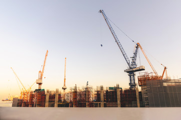 building construction site structure with crane silhouette at sunset against orange sky in city.