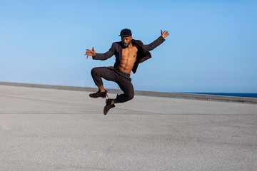 Front view young black man wearing casual clothes jumping in urban background.