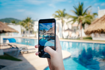 Wall Mural - hand holding phone on background of the pool in hotel. photo camera on the screen.