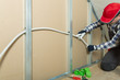 © artursfoto - Electrician at work - installing electricity wire into plasterboard wall in attic