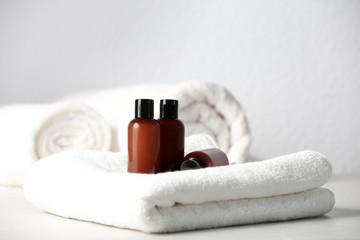 Wall Mural - Mini bottles with cosmetic products and towels on table against light background. Hotel amenities