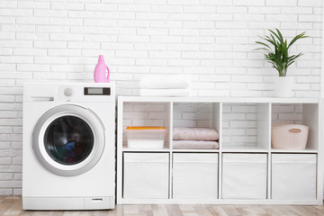 Modern washing machine near brick wall in laundry room interior