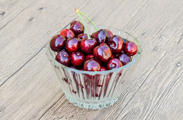 Berries of a sweet cherry in a glass bowl on a wooden background. Ripe red sweet cherry