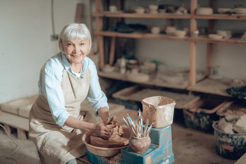 Waist up of elderly craftswoman making ceramic bowl in potter's studio