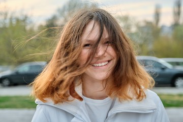 Outdoor portrait of teenager girl 15 years old, girl smiling with long brown hair in white jacket