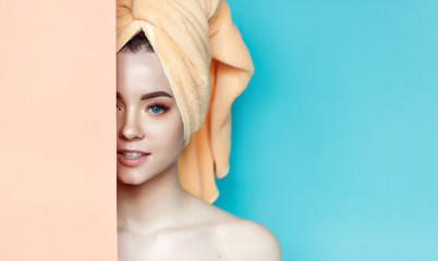 Portrait of young beautiful woman with healthy glow perfect smooth skin look into the hole of blue and orang paper. Model with natural nude make up with towel on head. Fashion, beauty, skincare.