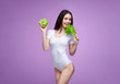 Beautiful slim brunette young girl in white lingerie. Purple background. Sporty healthy model posing with fresh green lettuce leaves, cabbage, cole. Diet, healthy food, nutrition, lifestyle concept.
