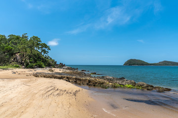 Cairns, Australia - February 18, 2019: North end of warm beige tropical beach and rocks of Palm Cove with azure Coral Sea water under blue sky. Double Island in back.