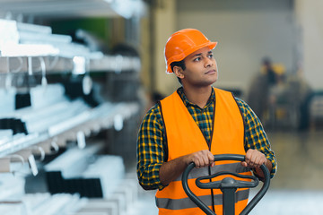 handsome indian warehouse worker standing near pallet jack and looking away