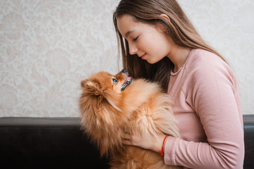 Teenage girl with a dog breed Spitz rejoices with a pet at home on the floor.