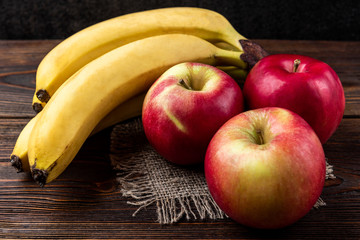 Banana and red apple on dark wooden background. 