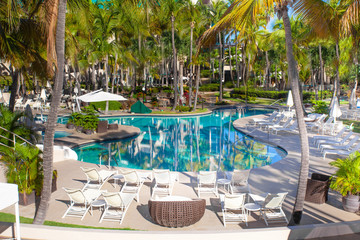 Beautiful swimming pool with palm trees and lounge chairs at unknown tropical hotel resort