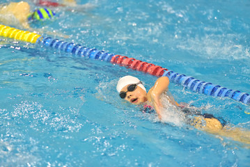 Young boy in goggles and cap swimming in the blue water pool