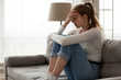 Upset woman frustrated by problem sitting on couch, embracing knees,