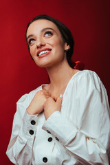 Beautiful portrait of young brunette woman with clear skin in white vintage blouse smiling while posing in a studio isolated on red background. Fashion portrait. Close up