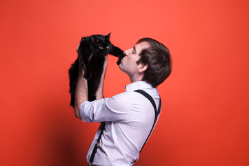 side view of man holding and kissing on paw black cat on orange background