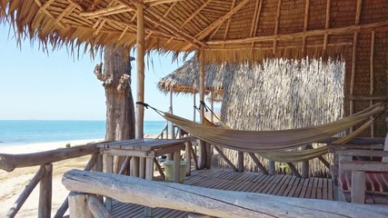 Wall Mural - View of sand beach with rocks at tropical island and bungalow with hammocks and wooden furniture. 4K clip