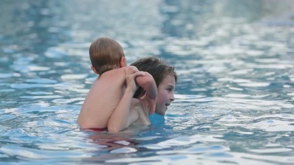 Wall Mural - Adorable happy little child, toddler boy, having fun relaxing and playing with his older brother in a pool on sunny day during summer vacation in resort