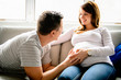 © Louis-Paul Photo - A happy man with pregnant woman sitting on couch