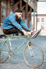 Wall Mural - Stylish man as a crazy hipster having fun, riding retro bicycle outdoors on the industrial urban background