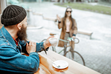 Wall Mural - Stylish man meeting his girlfriend with bicycle while sitting with coffee near the window at the cafe