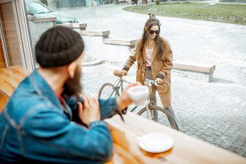 Wall Mural - Stylish man meeting his girlfriend with bicycle while sitting with coffee near the window at the cafe