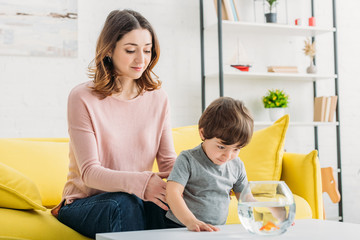 Wall Mural - cute curious boy looking at aquarium with gold fish near smiling mother