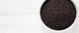 Fototapeta Kuchnia - Gluten-free raw organic black quinoa in a bowl over white wooden background, top view. From above, overhead, flat lay. Copy space.