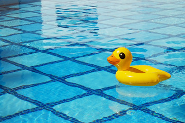 Top view of inflatable duck floating in an empty swimming pool with crystal clear water and blue square tile pattern background. Close up shot of rubber ring with a lot of copy space for text.