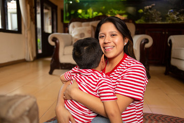 Wall Mural - mom hugs her 4 year old son while she smiles at the camera in her living room- siblings