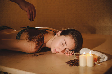 lateral view of a beautiful woman in spa salon having spa therapy with coffee done by a masseur