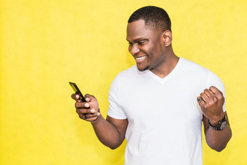 Happy African American man holding smartphone and celebrating his success.