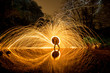 © Macia Puiggros/ADDICTIVE STOCK - Long exposure of silhouette of human with burning round and fireworks on rocks between water near mountains in evening