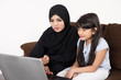 © Mahmoud Rahall - Arab woman teaching her daughter on laptop computer on white background