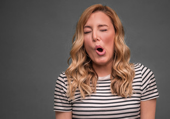 A young woman is squinting a sour grimace while standing against grey background.