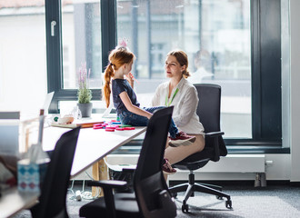 Wall Mural - A businesswoman with small daughter sitting in an office, working.