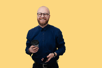 Wall Mural - Portrait of bearded man with spartphone and coffee in hands, looking and smiling at camera