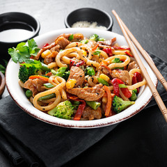 Wall Mural - Udon stir fry noodles with pork meat and vegetables in a white plate on black stone background.