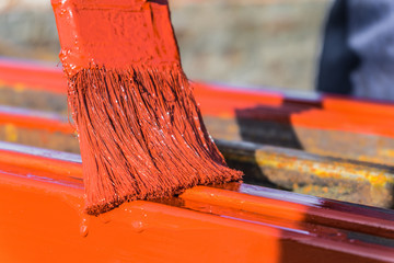 Paint application by brush on metal structures. Protective coating of steel closed profiles with primer iron oxide red.