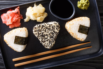 Wall Mural - Onigiri in sesame served with ginger, wasabi and sauce close-up on a plate. horizontal top view