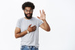 © Cookie Studio - You have my word. Portrait of charming confident, smiling african american man giving promise raising hand and holding arm on heart as giving oath or pledge, swearing not lie over gray background