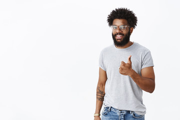 Nice job mate. Portrait of satisfied joyful and charismatic african-american bearded guy with curly hair, pierced nose and tattoos showing thumbs-up gesture and smiling delighted with good result