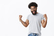 © Cookie Studio - Yeah feeling courage and readiness to achieve success. Confident and delighted optimistic african american bearded man raising clenched fists in celebration, triumphing being happy with good result