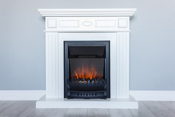 White wooden decorative electric fireplace with a beautiful burning flame. Interior photo on gray background.