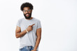 © Cookie Studio - Better go there. Portrait of delighted nice charming african american strong man with curly hair, piercing and tattoos smiling friendly at camera as pointing right inviting come in to his place